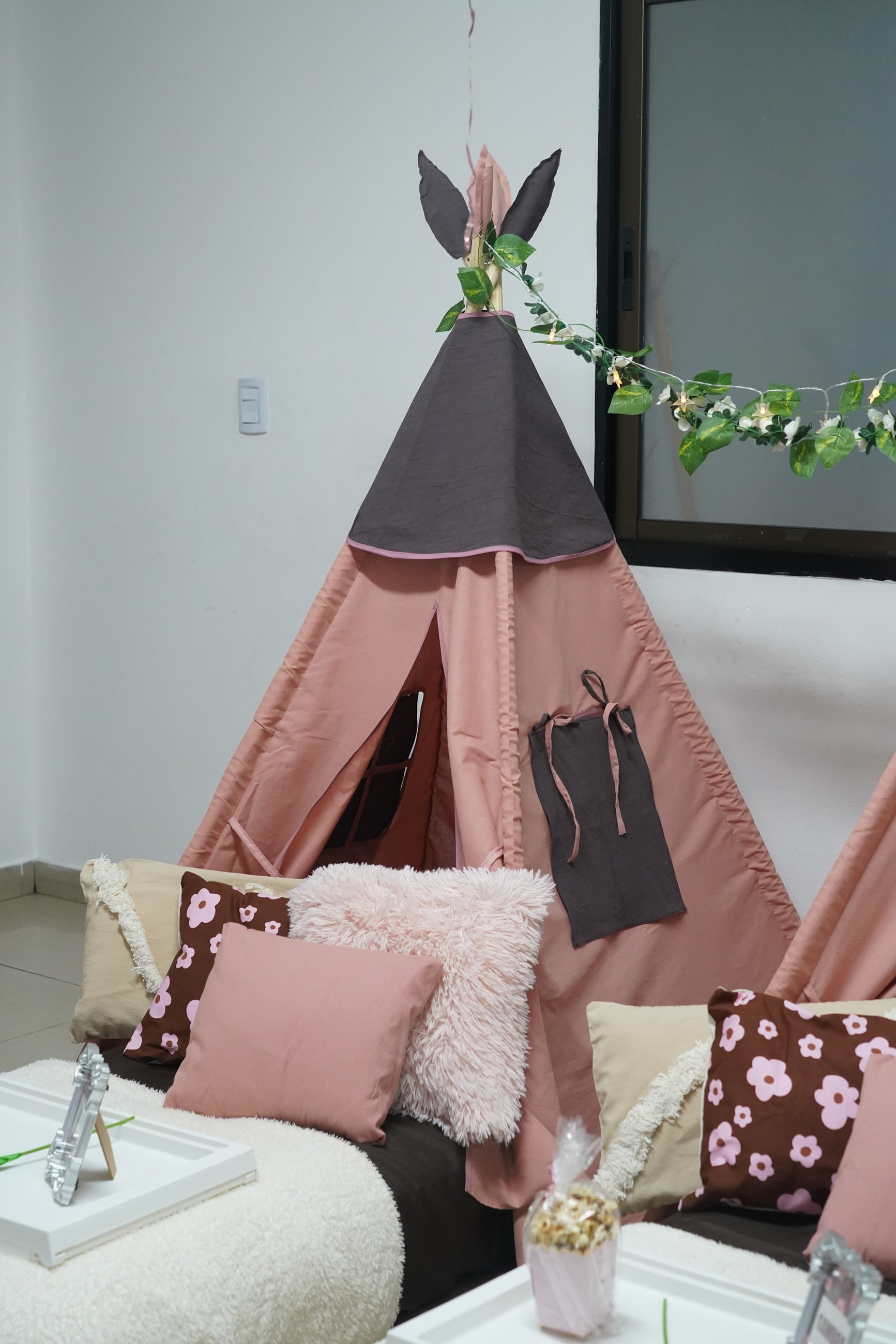 Una carpa tipi rosa con guirnalda de hojas y almohadones mullidos, floreados y lisos.