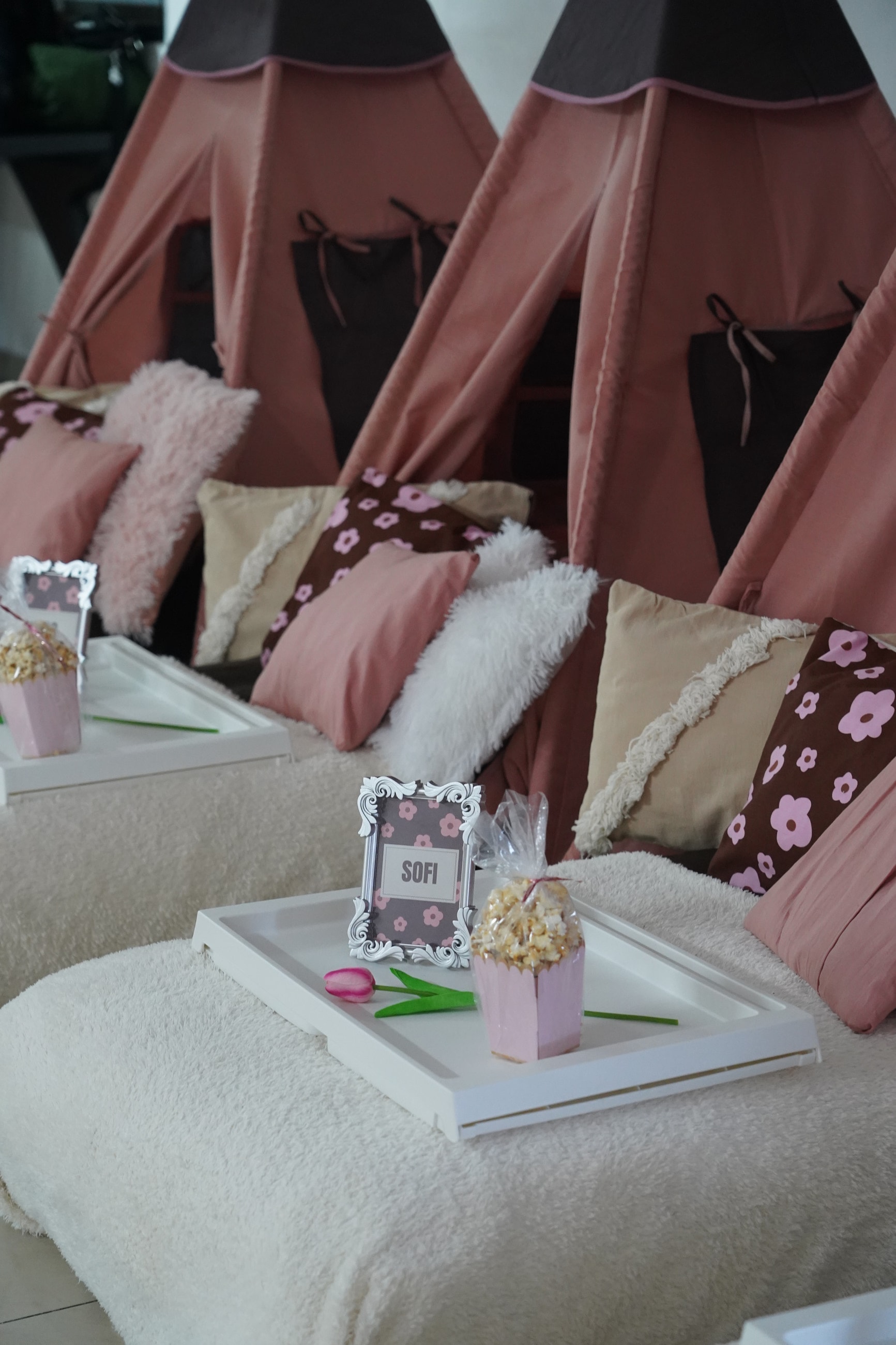 Hilera de carpas tipi rosa y chocolate con almohadones y bandejas sobre colchones blancos.