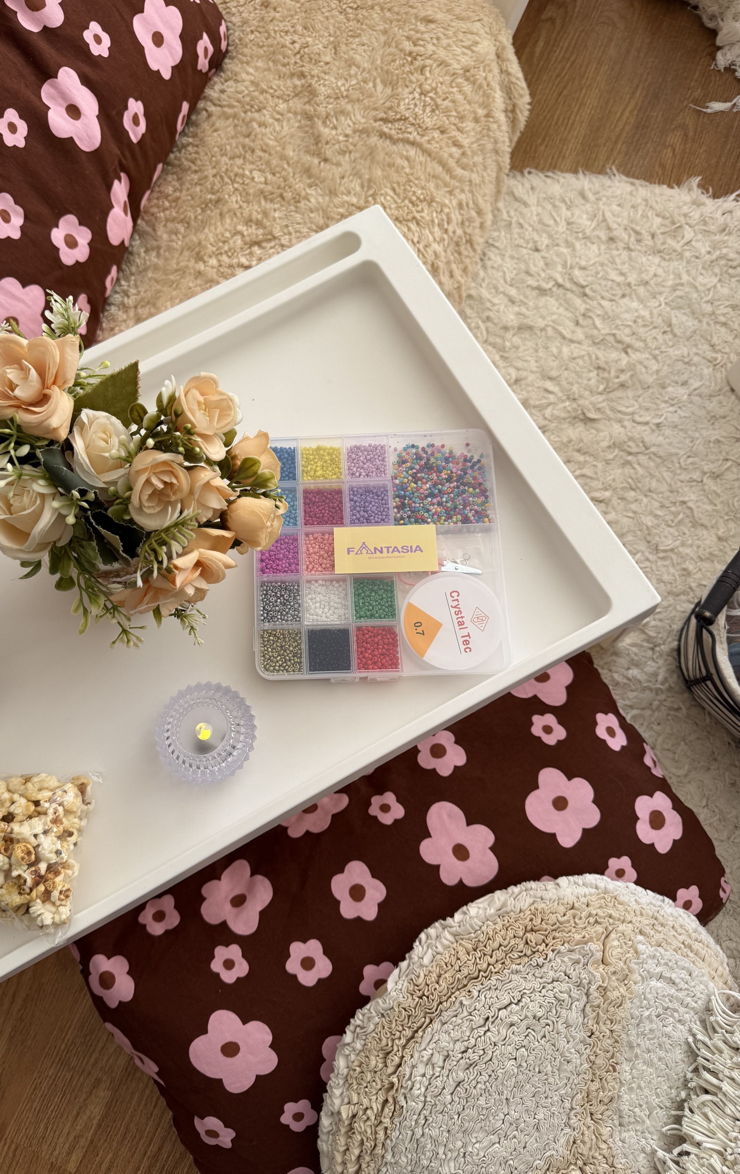 Bandeja con una caja de canutillos de colores, tanza elastizada, flores y pochoclos sobre almohadones floreados.